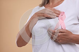 Breast cancer awareness. Woman with pink ribbon doing self-examination on light brown background, closeup. Space for text