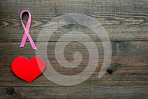 Breast cancer. Mammalogy concept. Symbolic pink ribbon near heart sign on dark wooden background top view copy space