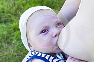 Breast-feeding. Close up portrait of baby who sucks milk from mother`s breast in nature.