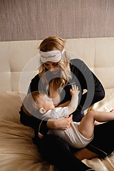 Breast feeding: Young blonde mother breastfeeds her baby boy child in bedroom wearing black sleeping robe costume - Son