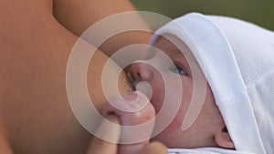 Breast feeding: Young mother breastfeeds her baby boy child in city park sitting on a bench wearing bright red dress -