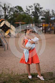 Breast feeding: Young mother breastfeeds her baby boy child in city park standing wearing bright red dress - Son wears
