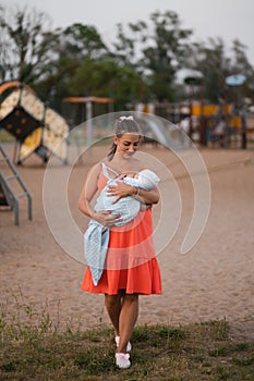 Breast feeding: Young mother breastfeeds her baby boy child in city park standing wearing bright red dress - Son wears