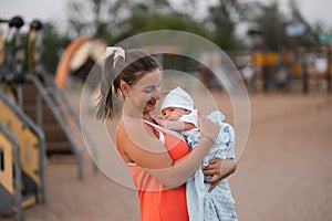 Breast feeding: Young mother breastfeeds her baby boy child in city park standing wearing bright red dress - Son wears