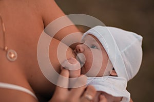 Breast feeding: Young mother breastfeeds her baby boy child outdoors wearing bright red dress - Son wears white cap -