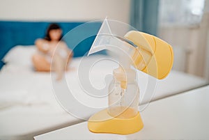 breast pump against background of blurred mother nursing baby with breast milk.