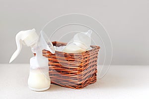 Breast pump and bottle with milk for baby in a straw basket. Free copy space.