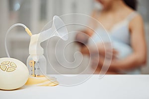 breast pump with breast milk against the background of a mother holding child.