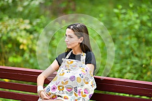 Breastfeeding a baby outdoors. A mother breastfeeds her newborn baby in the park on demand, sitting on a bench under the trees, in