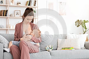 Breastfeeding Concept. Young woman lactating her toddler baby on couch at home