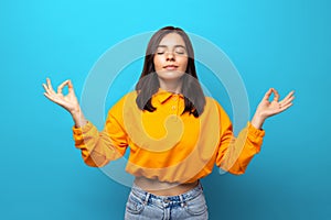 Breathe in. Beautiful multiethnicity woman in orange shirt getting zen calm against blue background