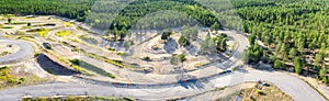 Breathtaking Aerial Panorama of Scandinavian green pine tree forest and part of speedway training track below. Sunny summer day.