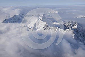 Beautiful aerial view of snow capped mountain peaks above clouds