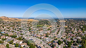 A breathtaking aerial view of Antioch, California: houses nestled amidst verdant hills, crisscrossed by meandering streets, all