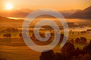 Breathtaking morning lansdcape of small bavarian village covered in fog. Scenic view of Bavarian Alps at sunrise with majestic mou