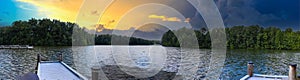 A breathtaking panoramic shot of the rippling waters of the lake with a long gray wooden dock over the water