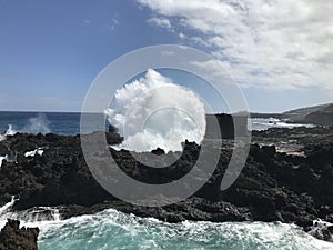 Breathtaking shot of a spray of water coming out of blowhole in rocks under a blue sky