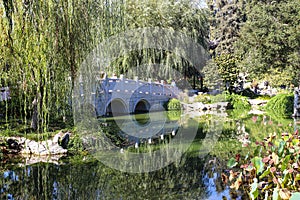 A breathtaking shot of a a stone bridge over a like with deep green lake water and lush green trees reflecting off the lake with b