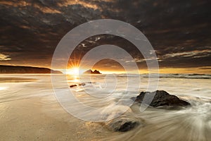 Breathtaking susnet from the dark sky over the fizzy water in Holywell Bay, Cornwall, UK