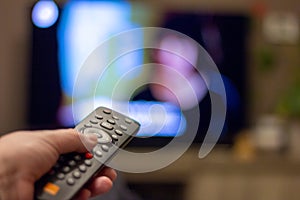 Brecht, Belgium - November 14 2019: A hand holding a television remote control with in the background a tv displaying a blurred