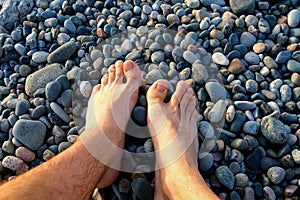 Brefooted tourist man's legs rest relax on pebble stone sea beach on vacation.