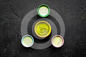 Brew matcha tea. Bowl with powder and cups with beverage on black background top view copy space