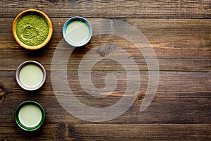 Brew matcha tea. Bowl with powder and cups with beverage on dark wooden background top view copy space