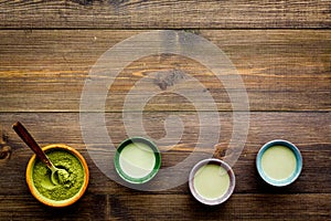 Brew matcha tea. Bowl with powder and cups with beverage on dark wooden background top view copy space