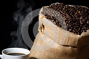 Brewed coffee in a white cup with steam or vapor and coffee beans in a burlap hessian sack in the background.