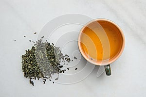 Brewed Green Tea in Ceramic Cup. Loose Leaves Scattered on White Marble Stone Background. Chinese Japanese Asian Cuisine