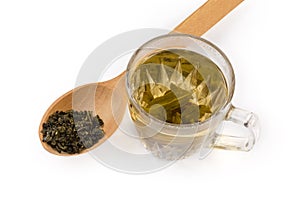 Brewed green tea in glass cup against dried tea leaves