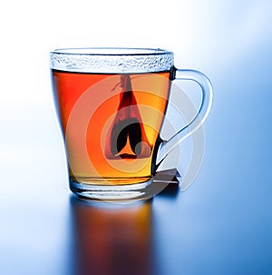 Brewed tea with a bag in a cup. High contrast. Saturated colors. White-blue background. Deep shadow.