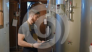 The brewer on the background of beer tanks makes calculations