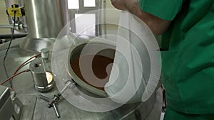 A brewer in green work clothes adds ingredients to a tank