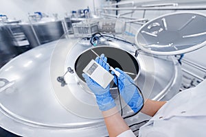 Brewery, female engineer checks temperature of a steel tank with wort. Industrial food worker concept