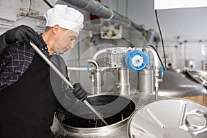 Brewery worker stirring raw materials in fermenter for beer production