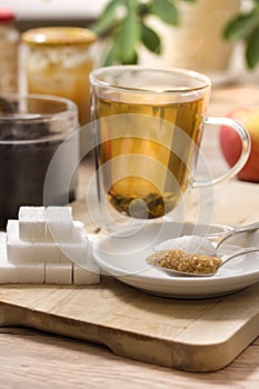 Brewing green tea in a glass. In the foreground white sugar, cane sugar and lump sugar.