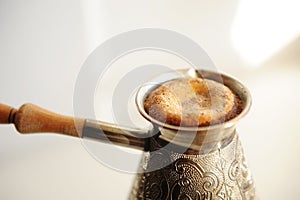 Brewing turkish coffee in cooper cezve. Rising foam close up. White background