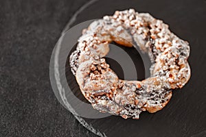 Brezel handcrafted sweet with nuts, on slate stone plate round, dark background, selective focus