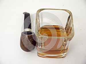 Briar smoking pipe near a glass of whisky close view with white