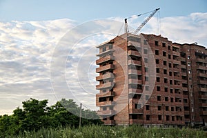 Brick apartment building on construction site with green territory and blue sky. Building process in town suburbs. Apartment