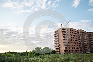 Brick apartment building on construction site with green territory and blue sky. Building process in town suburbs. Apartment