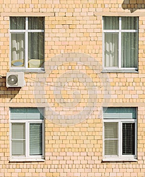 Brick apartment building sunny facade wall with its plastic windows with jalousies, curtains and air conditioner