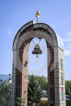 A brick arch with a bell and a spire near the Temple of All Religions in Kazan, Russia