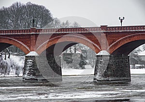 Brick arch bridge over the River. Modern architecture in Europe. Winter nature.