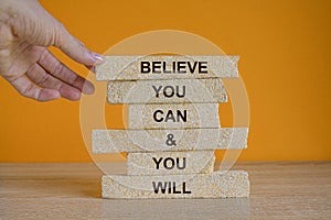 Brick blocks with message Believe You Can And You Will. Beautiful wooden table, orange background, copy space. Business