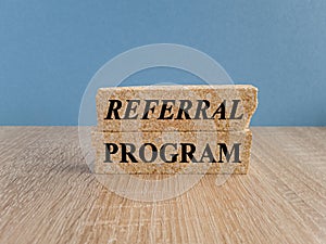 Brick blocks with text REFERRAL PROGRAM. Beautiful blue background, wooden table. Business concept