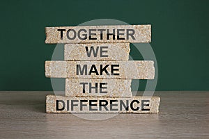 Brick blocks with words TOGETHER WE MAKE THE DIFFERENCE. Beautiful green background, wooden table. Business concept