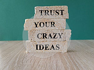 Brick blocks with words trust your crazy ideas. Beautiful wooden table, green background.