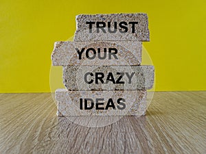 Brick blocks with words trust your crazy ideas. Beautiful wooden table, yellow background.